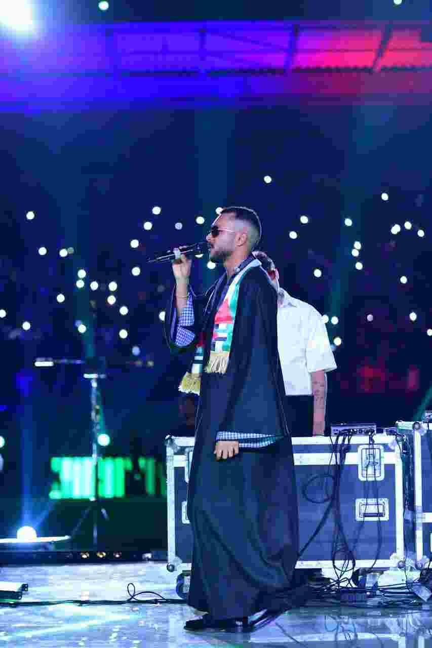 He wears a Palestinian jalabiya and shawl at a Benghazi concert.